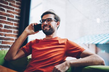 Sakallı smartphone aygıt üzerinde arama olumlu hipster adam arkadaşıyla görüşme ayarlamak için. Şık gözlük modern cep telefonu kafede oturan iç konuşurken neşeli genç adam