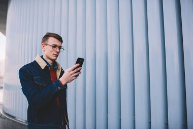Genç adam smartphone aygıt yolu ile 4 g web sitelerinde video izleme şık denim ceket giymiş konsantre promosyon arka plan tanıtım alanı ile birlikte kentsel ortamda gezinme Internet