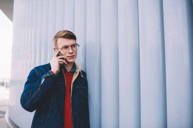 Smartphone üzerinde arama ve mobil faydaları işleci ile görüşmesi sırasında tartışırken rahat giyimli genç adam. Telefon ayakta duvarının yakınında kentsel ortamda konuşurken kot ceketli hipster çocuk