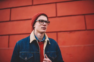 Kırmızı şapka ve şık optik gözlük planları kentsel ortamda yürüyüş sırasında düşünme düşünceli genç yakışıklı adam. Düşünceli hipster adam fikir ayakta yakınındaki promosyon arka plan üzerinde durulması