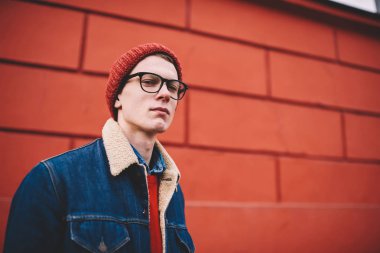 Ciddi hippi adam yarım uzunluk portre açık havada promosyon arka plan kopyalama alanı alanı ile birlikte kentsel ortamda gezinme sırasında kameraya bakarak şık denim ceket ve kırmızı şapka giymiş