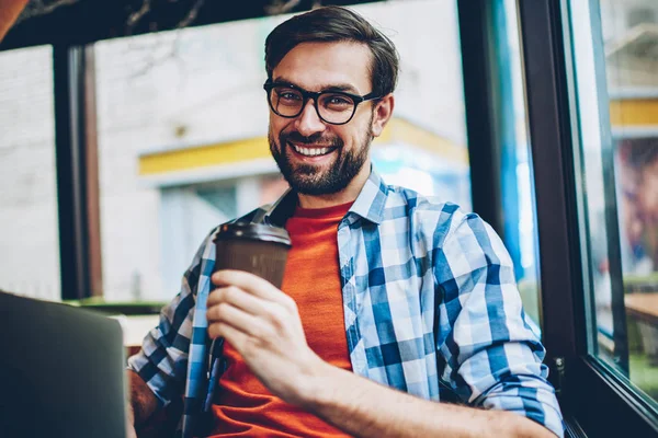 Yarım uzunluk portre mutlu yakışıklı el ve kameraya gülümseyen gitmek için kahve tutan gözlük öğrenci sakallı. Uzay coworking dinlenme içecekler ile olumlu erkek blogger