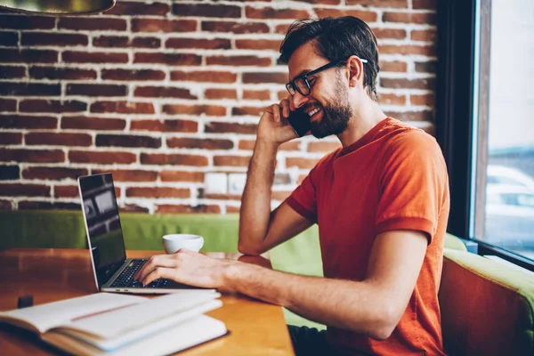 Sidovy Positiva Skäggig Ung Man Talar Smartphone Enhet Medan Skriva — Stockfoto