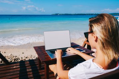 Genç kadının sahte ekran, kadın blogger izlerken videoda netbook dizüstü bilgisayarınızla ve takipçileri ile hafta sonları sohbet yazarak güzel okyanus plaj mesafe çalışmalarına arkadan görünüm