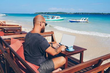 Online onun iş dizüstü bilgisayar üzerinden çalışırken okyanus kıyısında dinlenme, bin yıllık hipster adam güncelleştirme içeriği gezi hakkında yayın klavye içinde onun blogg yetenekli erkek serbest meslek