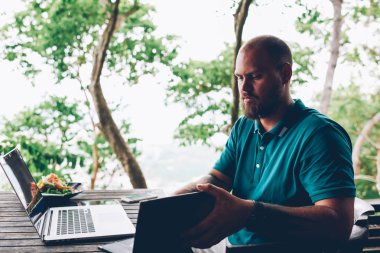 Ciddi beyaz adam açık Asya kafe Teras, düşünceli erkek blogger wifi bağlantı için uzak iş kullanarak salata için fatura kontrol uzak iş dizüstü bilgisayar ile oturup yemek yemek için seyir menü