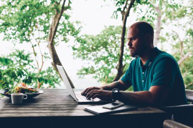 Asya kafe Teras, dizüstü bilgisayar üzerinden uzak iş görev yaparken ciddi bin yıllık iş adamı serbest çalışan web sayfasında yayınlanması için makale yazarak üzerinde konsantre yaratıcı erkek blogger