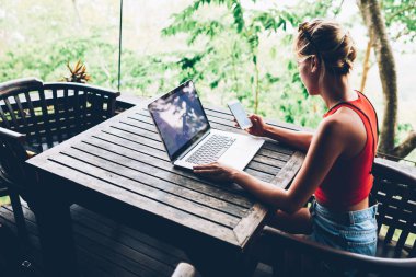 Kadın holding Smartphone arkadan görünüm uzaktan çalışma tatil sırasında kafe teras üzerinde oturan serbest iş için dizüstü bilgisayar ve wifi bağlantısı kullanan kadın gelir iletisi hakkında bildirim almak 