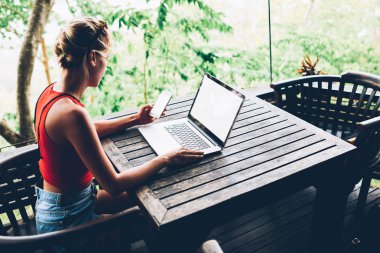 Genç hippi kız paylaşım web sayfasında dizüstü bilgisayar, bin yıllık kadın serbest meslek sahibi uzak iş ve bloglama için Wi-Fi bağlantısı kullanarak üzerinden rezervasyon yapma smartphone app üzerinden para işlem yapma