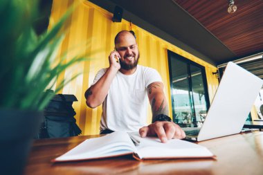 Not defteri paylaşım bilgileri cep telefonu konuşma sırasında notlarda işaret eden neşeli hipster adam. mutlu erkek öğrenci üniversite kampüsünün dizüstü bilgisayar ile oturup ödev hakkında danışmanlık arkadaş arama