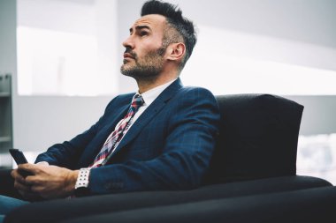 Düşünceli gurur Genel Müdür metin yanıt iletisindeki elinde smartphone ile kanepede oturan düşünürken arıyorum. Formal giyim cep ofiste sohbet olgun işadamı durulması