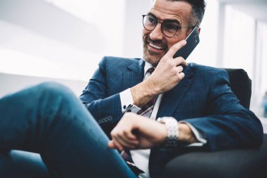 Başarılı bir girişimci orta yaşlı ofisinde oturan Smartphone cep telefonu ile telefon görüşmesi sırasında gülüyor. Zengin işadamı resmi aşınmaya cep telefonundan arıyorum. Neşeli gurur CEO'su cep üzerinde konuşuyor