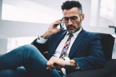 Zaman denetleme ve toplantı üzerinde bekleyen bir seyretmek ararken meşgul emin işadamı orta yaşlı istek-e doğru Smartphone cep telefonu ile ortak. Formal giyim üzerinde modern cep konuşurken gurur CEO'su deneyimli