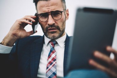 Kendine güvenen orta yarım uzunluk portre smartphone aygıtında çağrılırken kameraya bakarak girişimci yaşlı. Ciddi icra müdürü 50 yaşında elinde cep telefonu üzerinde konuşurken dokunmatik yüzey ile