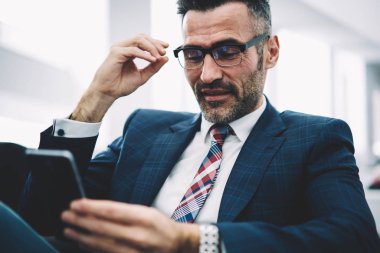 Neşeli olgun girişimci komik bildirim ofisinde oturan smartphone aygıt üzerinde okuma. Formal giyim online telefon aygıtı 4 g internet bağlantısı üzerinden sohbet başarılı gurur ceo