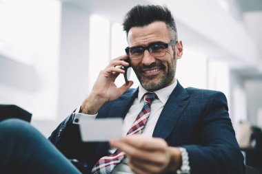 Müreffeh gurur CEO'su orta yarım uzunluk portre holding iş kartı elinde smartphone aygıtında çağrılırken yaşlı. Başarılı bir girişimci resmi modern cep telefonda konuşurken giymek