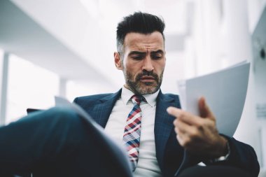 Dalgın emin gurur CEO'su oturma içinde yazıhane kağıt mali belgelerin incelenmesi formal giyim giymiş. Konsantre girişimci şık elbiseli muhasebe raporları bilgi veri okuma