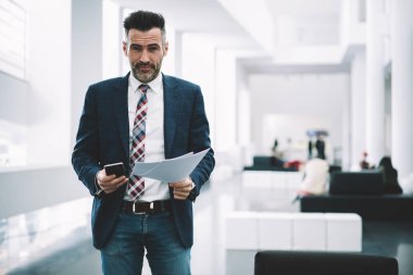 Orta yaşlı başarılı gurur CEO'su portresi finansal belgeler elinde tutarken kameraya gülümseyen formal giyim giymiş. Smartphone ayakta Office ile müreffeh icra müdürü