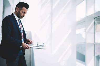 Kendinden emin ve başarılı orta yan görünüm yaşında gurur CEO'su formal giyim ayakta mali şirket ofisinde giyinmiş. Kopyalama alanı alanı yakınındaki belgeleri okuma takım elbiseli ciddi olgun işadamı