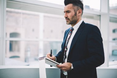 Not defteri ayakta Office programında aşağı ciddi erkek girişimci 50 yaşında yazma. Formal giyim Not Defteri'nde yaparken stratejisi geliştirme konusunda başarılı emin gurur CEO'su giymiş