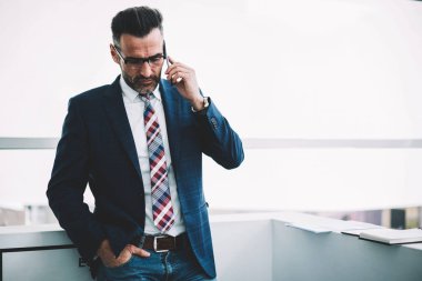 Formal giyim işleci ile hesaba dijital Smartphone'da bankacılık hakkında konuşurken giymiş ciddi orta yaşlı işadamı. Modern cep telefonundan arıyor takım elbiseli emin olgun girişimci