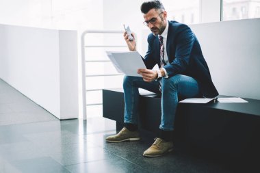 Dalgın olgun girişimci muhasebe raporları bilgi verilerle kontrol formal giyim giymiş. Ofis iç oturan deneyimli işadamı orta yaşlı okuma mali metin belgeleri