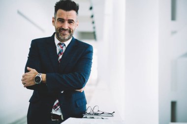 Yarım uzunluk portre mutlu olgun girişimci kameraya gülümseyen formal giyim giymiş. Başarılı bir iş adamı orta çapraz elle Office Kurumsal şirketin kopya alanı yakınında duran yaşlı