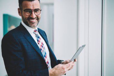 Yarım uzunluk portre resmi başarılı olgun işadamı giymek dokunmatik yüzey 4 g internet bağlantısı üzerinden ücret tahsil online yaparken kameraya gülümseyen. Tablet ile müreffeh gurur ceo