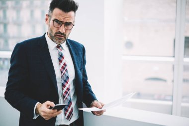 Yarım uzunluk portre emin olgun gurur CEO Smartphone'da kamera arama numarasına süre bakarak takım elbiseli. Hücresel kopya alanı yakınındaki posta kontrol belgeleri ile başarılı ciddi iş adamı