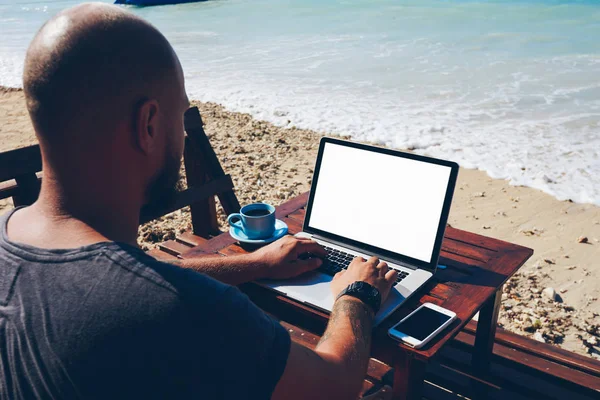 Arkadan görünüm yetenekli erkek Freelancer okyanus mesafe işi desteklemek dizüstü bilgisayarda tarama bilgilerini, adam deniz beac üzerinde Web sitesi yeniden yazarak blogger posta güncelleme içerik için seyahat