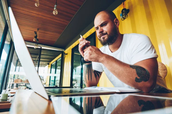 Pensive male student analyzing information for writing homework watching tutorial on laptop upset with bad connection, unhappy hipster guy waiting for software update for working on freelance