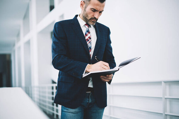 Pensive mature proud ceo dressed in formal wear writing down records in notepad developing business strategy.Concentrated businessman 50 years old signing financial documents of corporate company