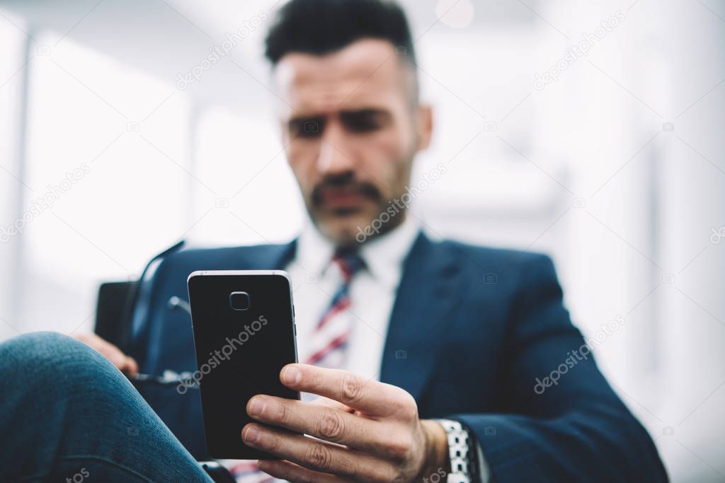 Selective focus on modern smartphone device with 4G internet connection in hands of mature businessman in formal wear.Blurred background of entrepreneur middle aged holding digital mobile phone
