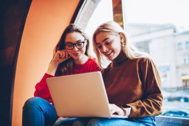 Pozitif kız öğrenci eğitim webinar birlikte kablosuz bağlantı ve dizüstü bilgisayar kullanarak coworking uzayda genç kız arkadaşlar eğlenmeye izlerken zevk netbook üzerinde boş zaman üzerinde ağ 