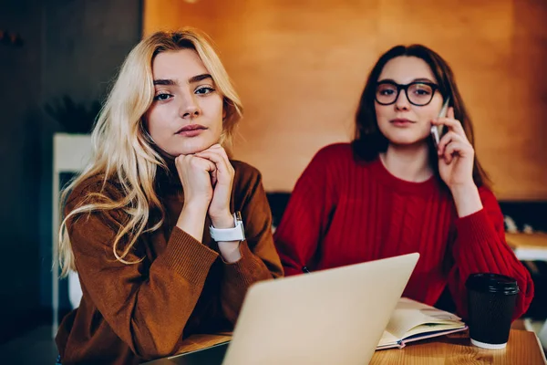 Portrait of serious female freelancers using modern technology during remote job in coworking office,young women earning money online doing distance job professionally together looking at camer