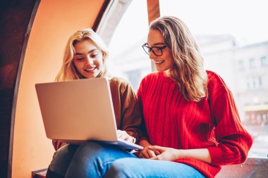 Web mağazası Cafe'de birlikte, video izlerken ve girintili coworking online kursları Öğrenme birbirleriyle konuşurken gülümseyen kız öğrenci dinlenme dizüstü bilgisayar üzerinden alışveriş pozitif hipster kızlar