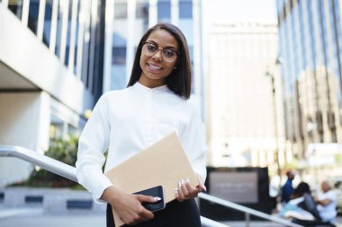 Gözlük vizyon düzeltme klasör Ofis Binası yakınındaki açık havada duran elinde modern smartphone ile tutarak kameraya gülümseyen müreffeh Afrikalı-Amerikalı kadın avukat portresi
