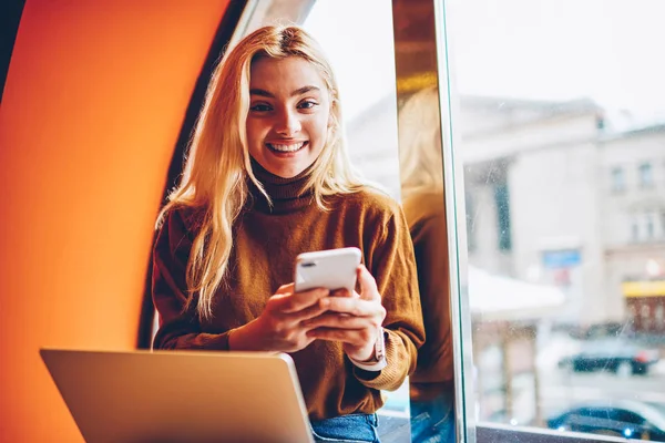 Portrait of cheerful hipster girl celebrating victory in online contest get email on smartphone, happy young woman excited popularity of publication in blog working on freelance in cafe on netbook