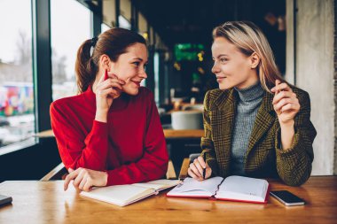 İki yaratıcı öğrenci işbirliği ile bloknot alan coworking içinde vasıl okul sırası oturan üretken strateji tartışıyor. Casual kıyafet birlikte ortak proje üzerinde çalışan kadın tasarımcılar gülümseyen