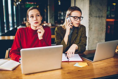 Dizüstü cihaz netbook oturan ortak tasarım Web sitesi geliştirmek için yaratıcı fikirler üzerinde düşünme hipster öğrenci iken teknik sorunu çözmek için hizmet için smartphone üzerinde arama sarışın genç kadın