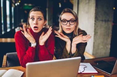 Yarım uzunluk portre karışık iki öğrenci bilgisayarda eğitim sorunu çözmek için bilmiyorum. Coworking yaklaşan sınavlar için hazırlarken kameraya bakarak omuz silkti hipster blogcular şaşkın