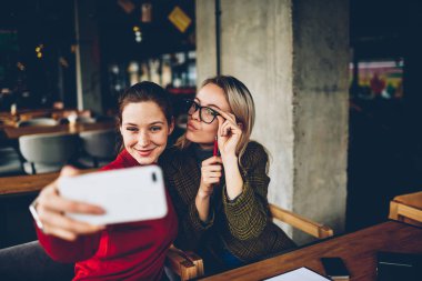 Casual giyim poz ve selfie fotoğraflar yayın için modern smartphone cep telefonu ile sosyal ağlar kafede dostu toplantı sırasında iç yapım komik suratlar ile iki başarılı kadın blogcular