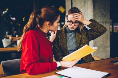 Nitelikli kadın öğretmen elinde yardımcı ders kitabı ile birlikte şık coworking alanda eğitim yaklaşan sınavlar için hazırlanması sırasında karışık eğitim malzeme anlamak için öğrenci depresif