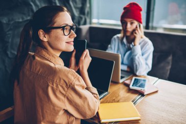 Uzak tutma smartphone elinde seyir ve modern netbook aygıt meslektaşım Smartphone'da söz ederken çalışan mutlu esmer öğrenci. Dizüstü bilgisayarlar kapalı oturan iki kadın serbest