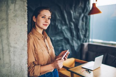 Düşünceli casual kadın blogger modern smartphone tutarak kendi web sitesi geliştirmek için yaratıcı fikirler üzerinde durulması giyinmiş. Planları coworking dururken düşünme düşünce hippi kız