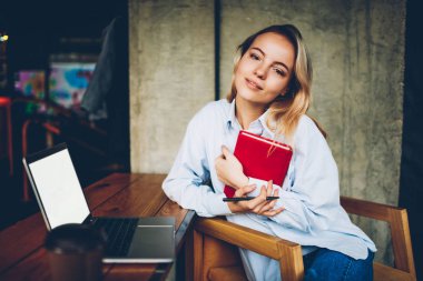 Not Defteri'nde eller liiking alan coworking içinde boş ekran alanı ile dijital netbook otururken kamera ile çekici sarışın hipster öğrenci portresi. Ders kitabı olan güzel kadın