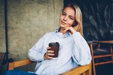 Yarım uzunluk portre sevimli sarışın kadın hipster Blogger lezzetli kahve içecek ve eğlence zamanı kapalı cafeterie iç tadını çıkarırken kameraya gülümseyen şık gömlek giymiş