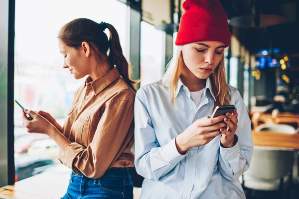 Antisocial hipster bloggers in stylish outfit messaging online in chat on smartphone device with 4G connection.Addicted young women ignoring live communication while updating profile on websites