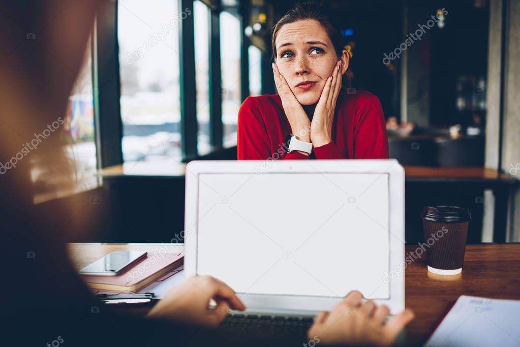 Puzzled female blogger thinking on solving problem and developing website working remotely while colleague typing information on keyboard of netbook with blank screen area for internet advertising
