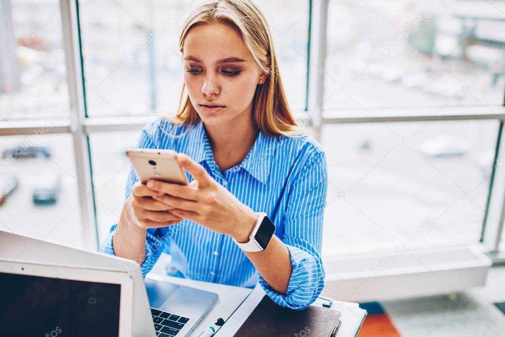 Serious female entrepreneur checking email box on smartphone texting feedback while spending time in office,businesswoman using application on smartphone for banking online making transaction